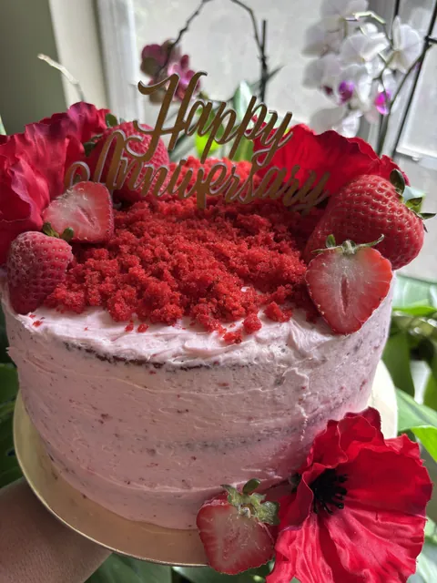 A pink anniversary cake crowned with red velvet crumb, strawberries and poppies