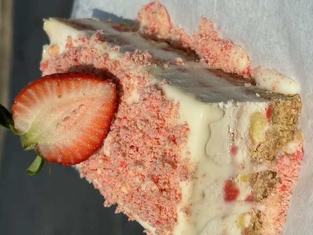A strawberry crunch cheesecake slice cut to show the layers, fresh strawberry on the side