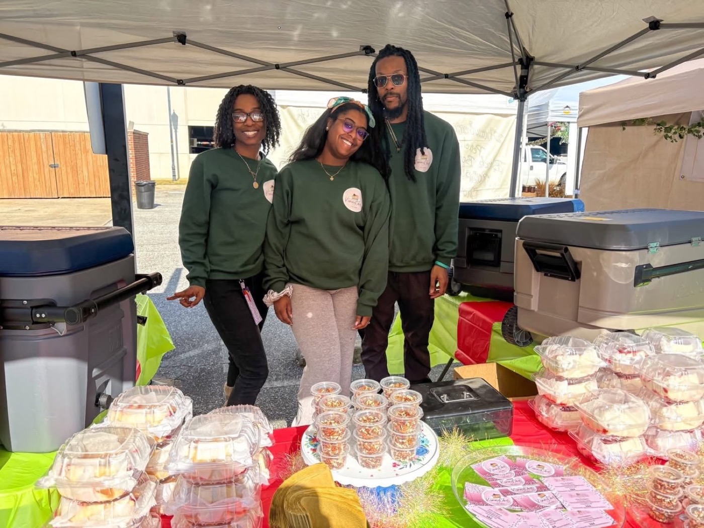 Us behind the Kimmy Cakes table at a market, boxed cheesecake and dessert cups laid out in front of us